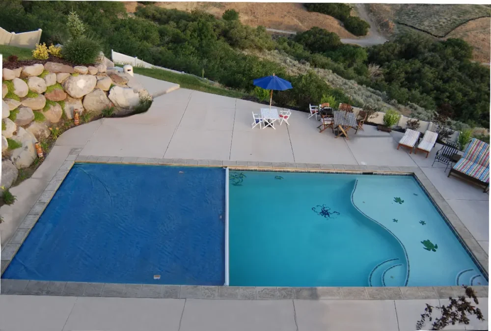 Photo of an automatic pool cover closed over half of an in-ground pool beside a stone retaining wall