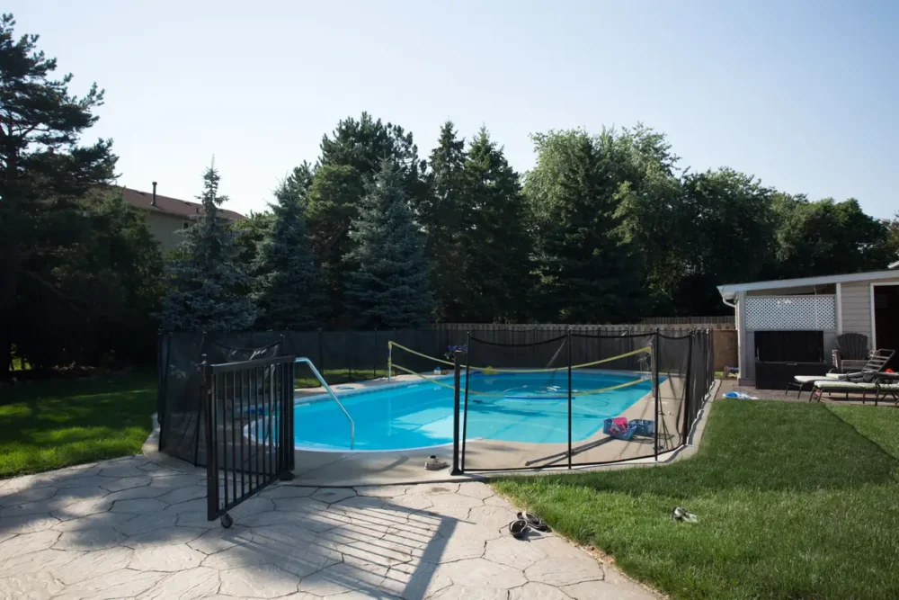 Photo of an in-ground backyard pool with clear blue water behind a black mesh safety fence
