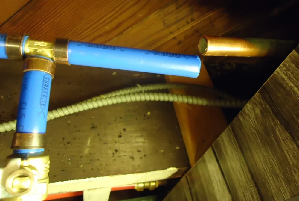 Photo of a basement ceiling with blue PEX and copper water pipes and a brass valve on an outdoor faucet line