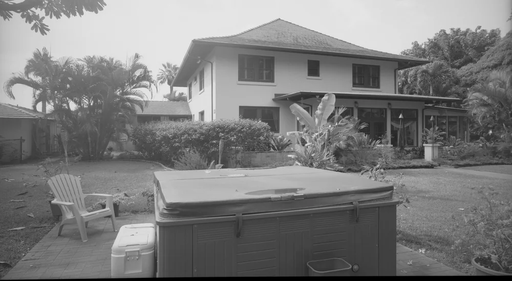 Black-and-white photo of a portable hot tub under a hard cover in a Honolulu backyard with palm trees