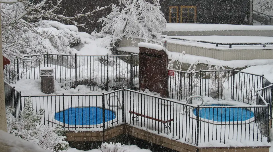 Photo of two round outdoor hot tubs behind an iron safety fence at an inn during a heavy snowfall