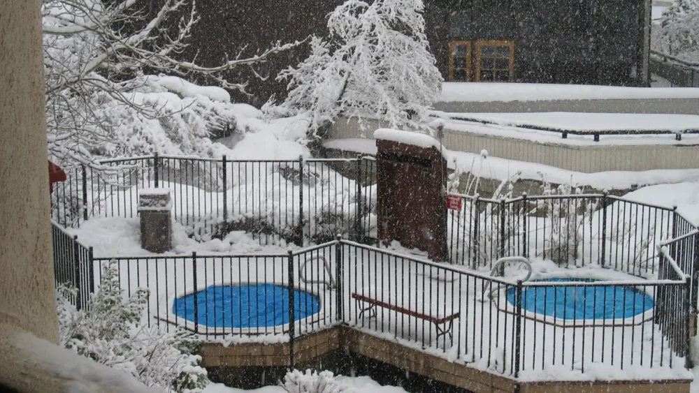 Photo of two covered hot tubs with blue lids inside a snowy fenced deck during a heavy snowfall