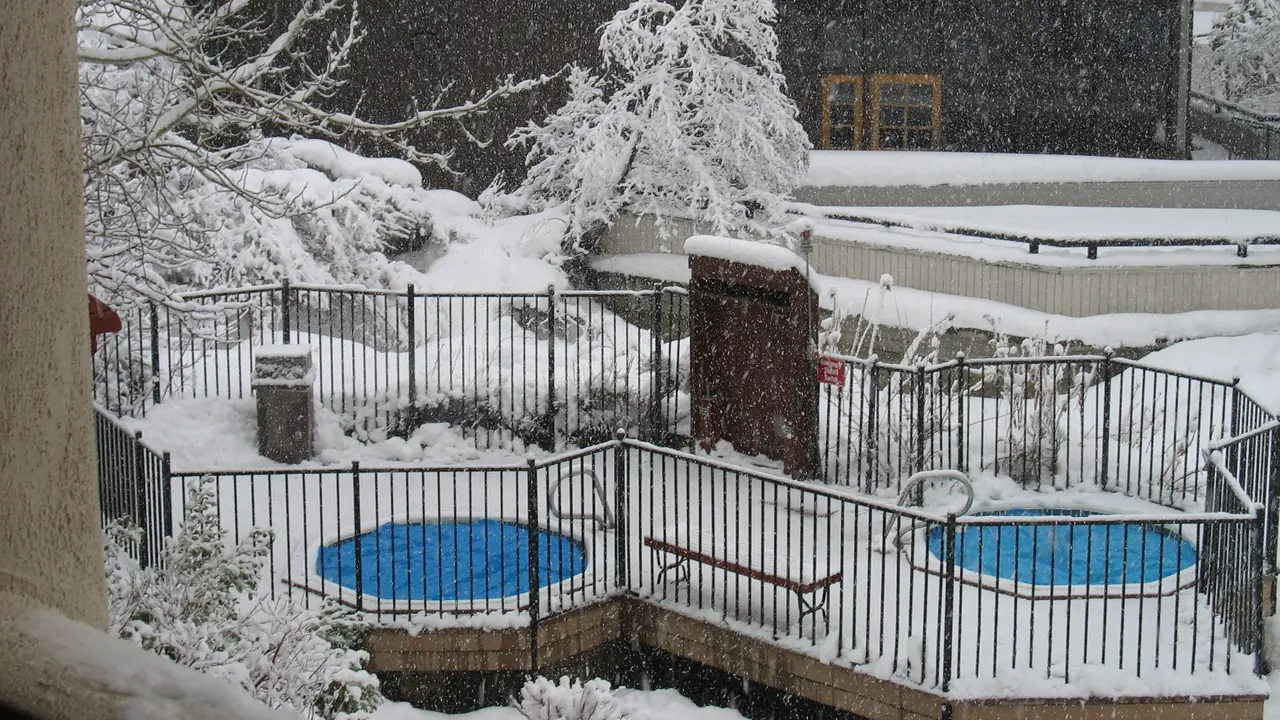 Photo of two covered hot tubs with blue lids inside a snowy fenced deck during a heavy snowfall