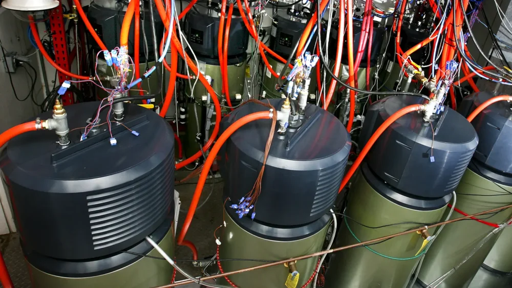 Photo of a row of electric water heaters wired with orange tubing and test sensors inside a laboratory chamber