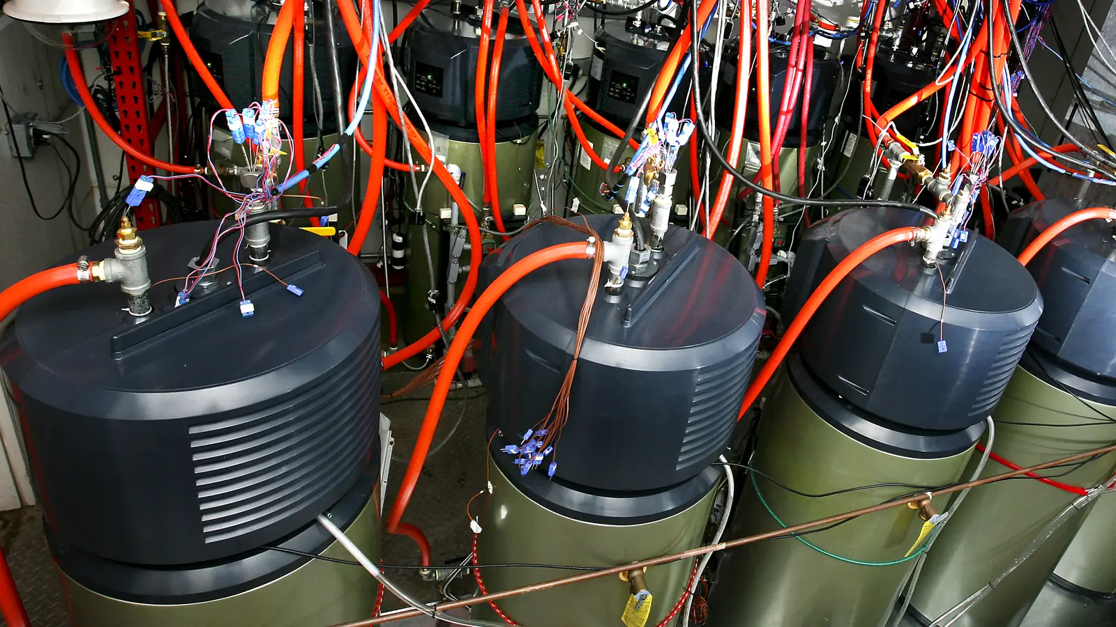Photo of a row of electric water heaters wired with orange tubing and test sensors inside a laboratory chamber