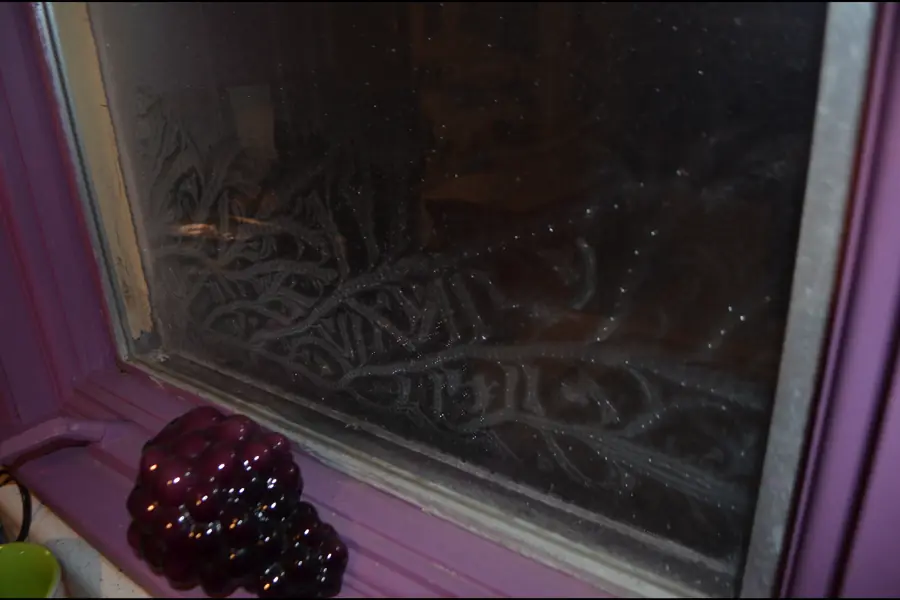 Photo of frost ferns covering a window pane above a purple painted sill in a northern January