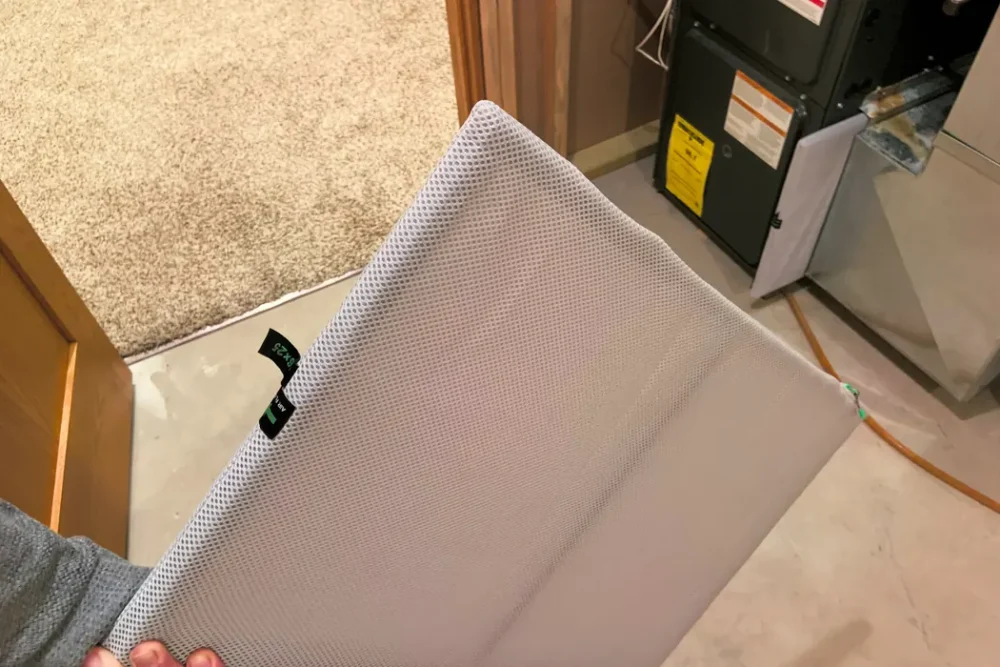 Photo of a reusable HVAC air filter held in front of a gas furnace in a basement utility area