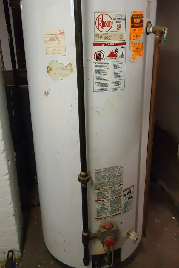 Photo of a white gas-fired tank water heater with a metal vent pipe and gas line in a basement