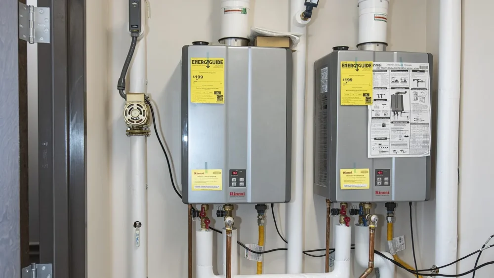 Photo of two wall-mounted gas tankless water heaters with vent pipes, gas lines and EnergyGuide labels in a utility room