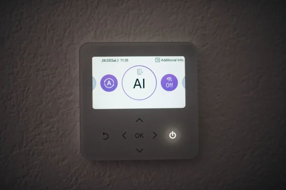 Photo of a wall-mounted heat pump controller with a lit display screen and arrow buttons below it