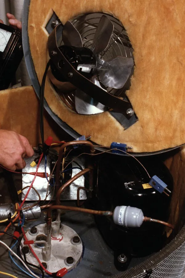 Photo of an opened early heat pump water heater showing its fan, compressor and copper tubing above the tank