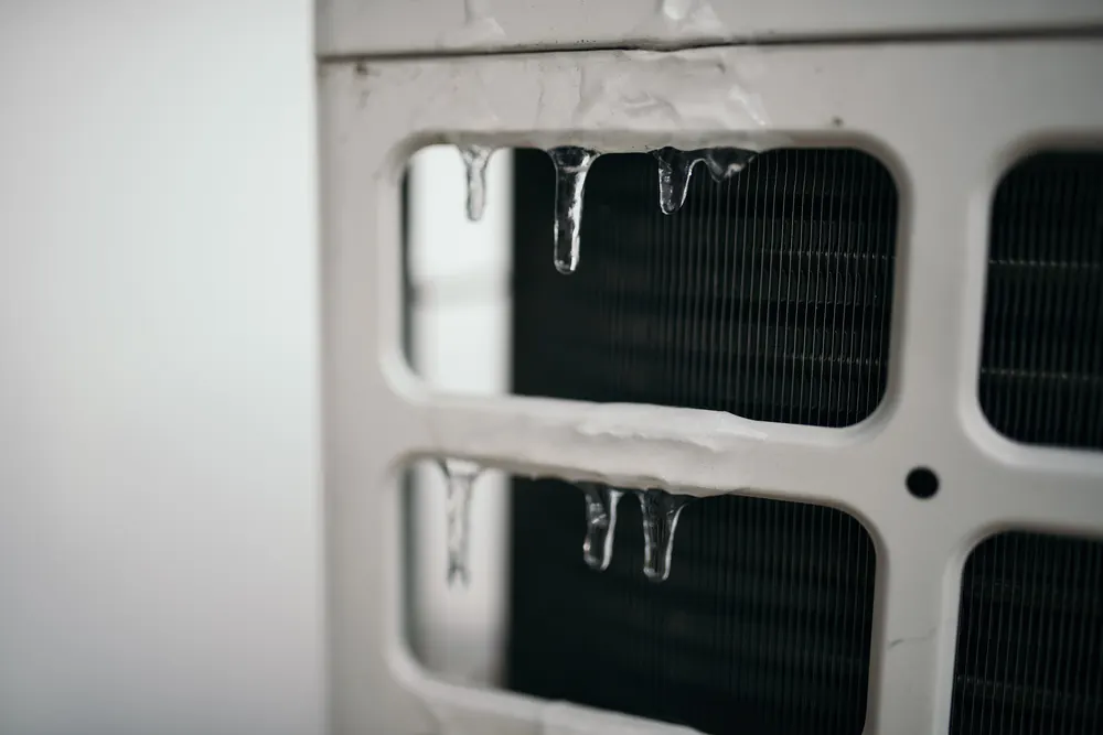 Close-up photo of icicles hanging from the coil guard of a heat pump outdoor unit in winter