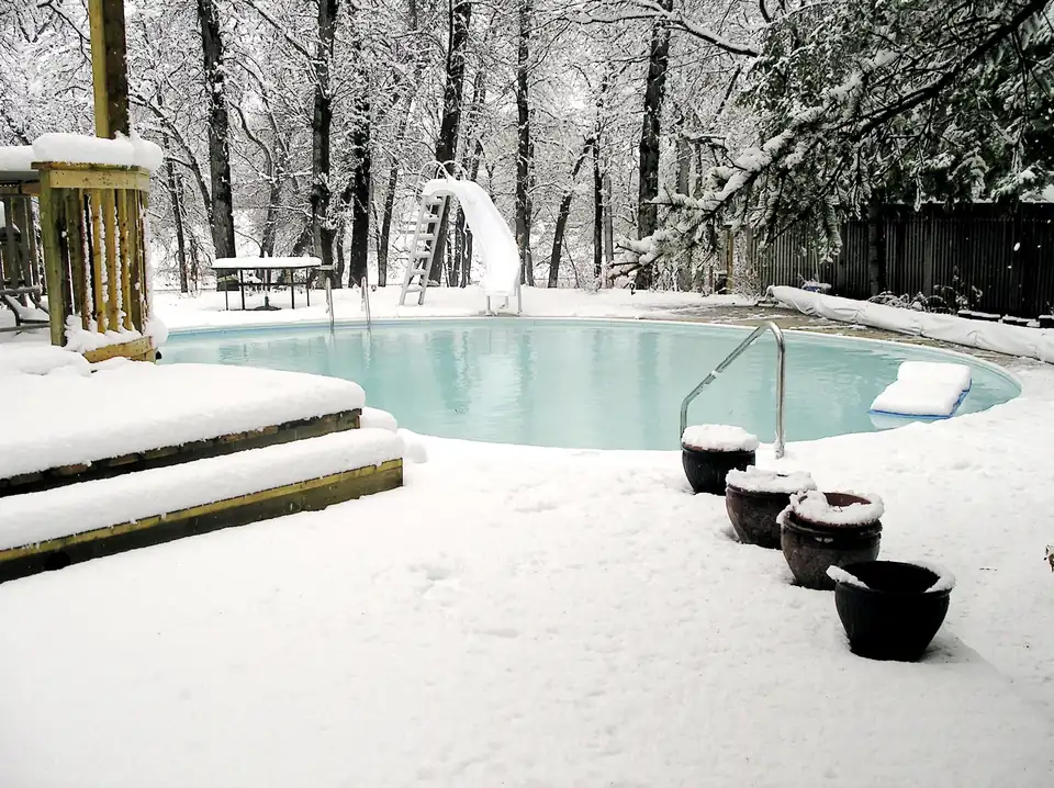 Photo of an open in-ground pool with a slide, surrounded by fresh snow after a late spring storm