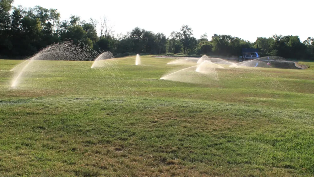 Photo of a lawn sprinkler system spraying arcs of water across a wide green lawn in Michigan