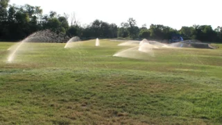Photo of a lawn sprinkler system spraying arcs of water across a wide green lawn in Michigan