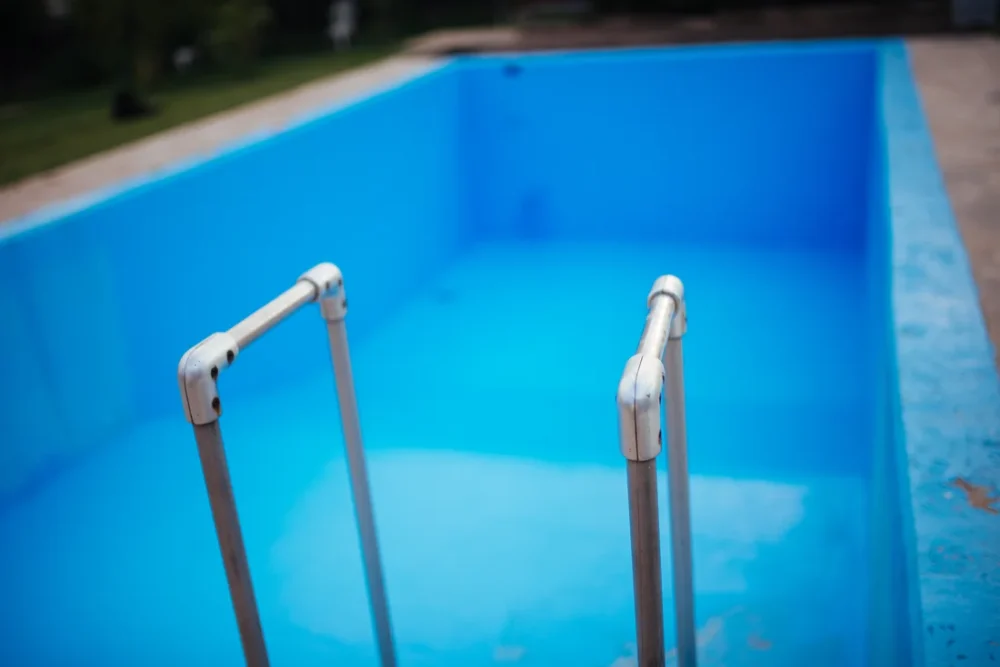 Photo of two stainless steel ladder rails at the edge of an empty blue in-ground pool before filling