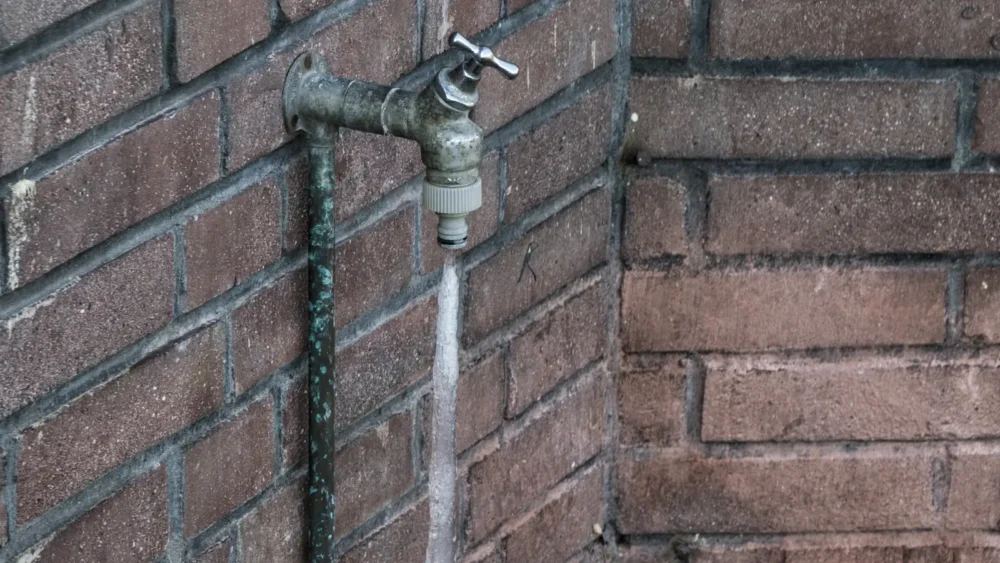 Photo of an outdoor faucet on a brick wall with the water below its spout frozen into a column of ice