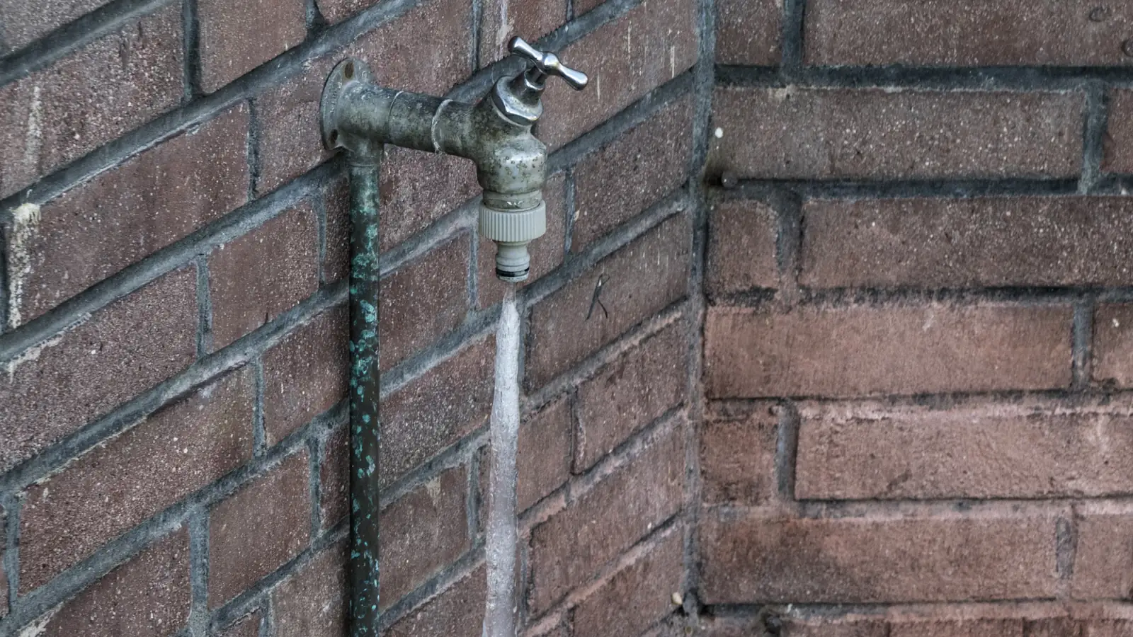 Photo of an outdoor faucet on a brick wall with the water below its spout frozen into a column of ice