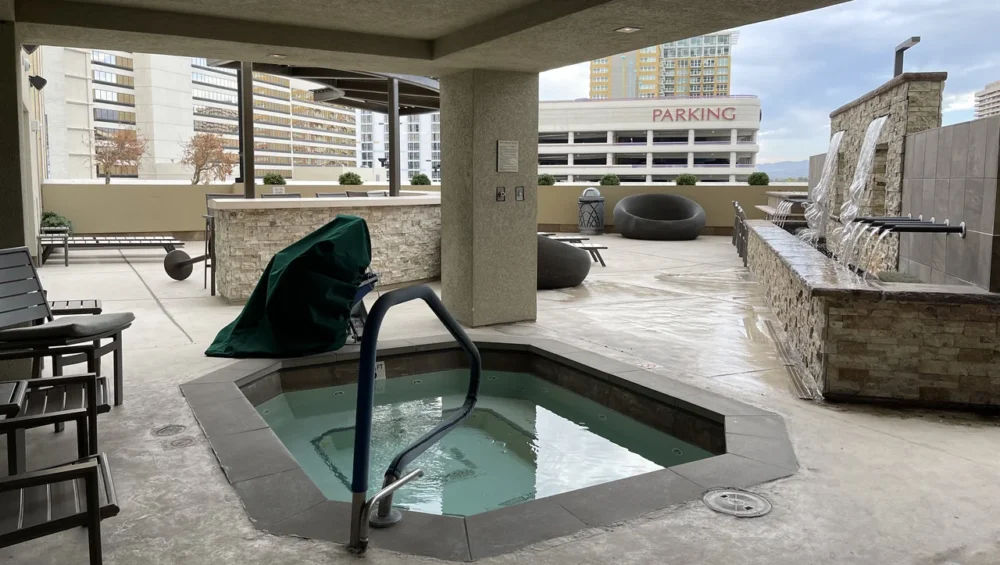Photo of an empty outdoor hotel hot tub with clear water, a handrail and a covered lounge area behind it
