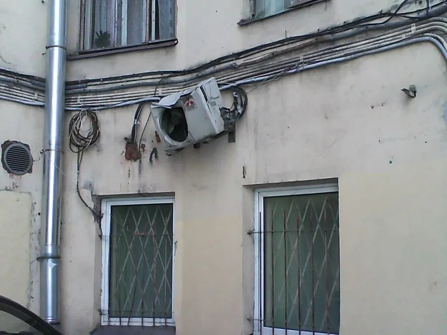 Photo of a wall-mounted outdoor unit on an old building, its casing crushed from above, likely by falling ice