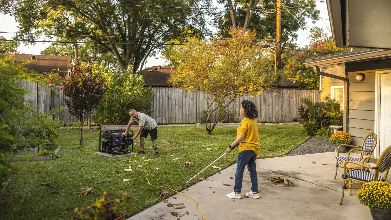 Photo of a portable generator running out in a backyard, far from the house, with a yellow cord across the lawn