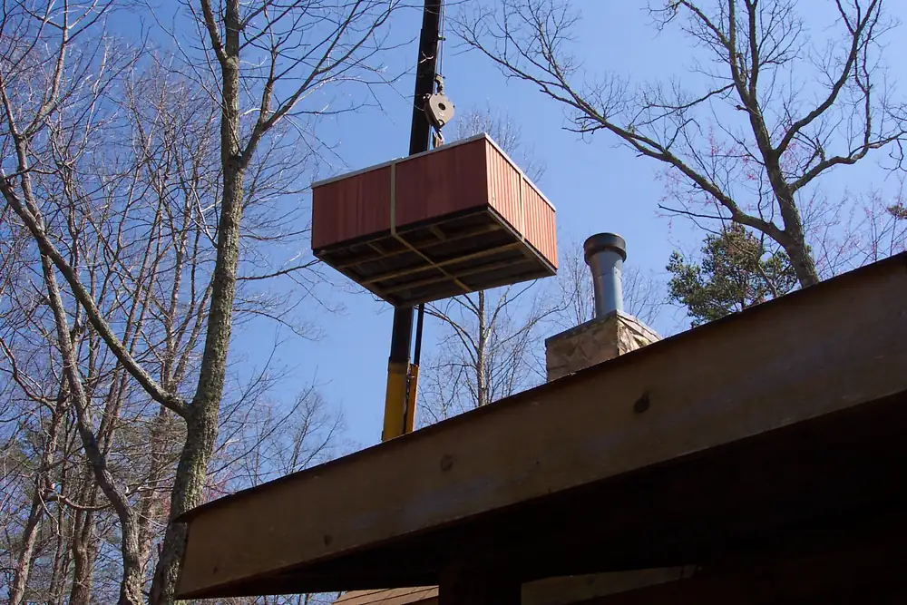 Photo of a portable hot tub cabinet lifted by a crane over a cabin roof toward its deck