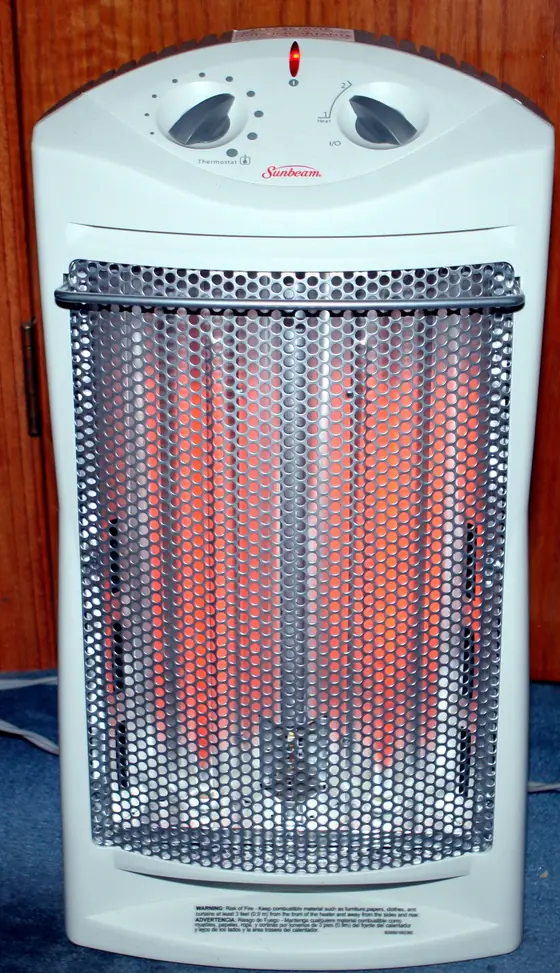 Photo of a white quartz space heater with thermostat dials and a printed fire-risk warning label on its base