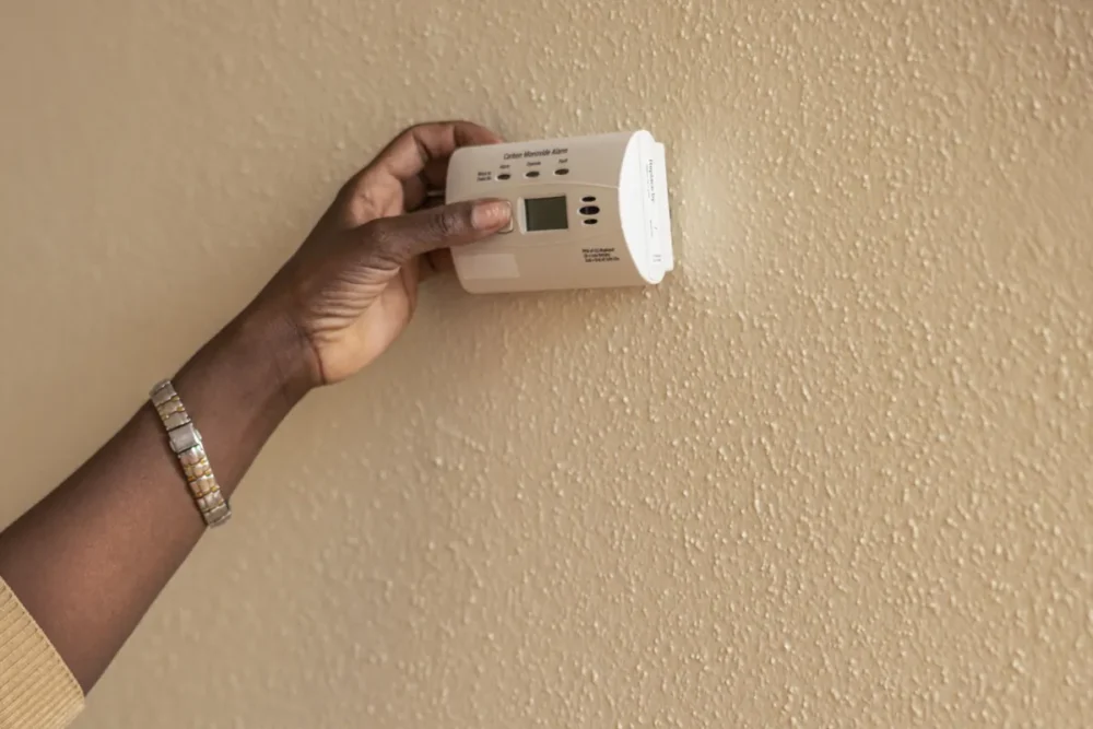 Photo of a hand pressing the test button on a battery carbon monoxide alarm mounted on a wall